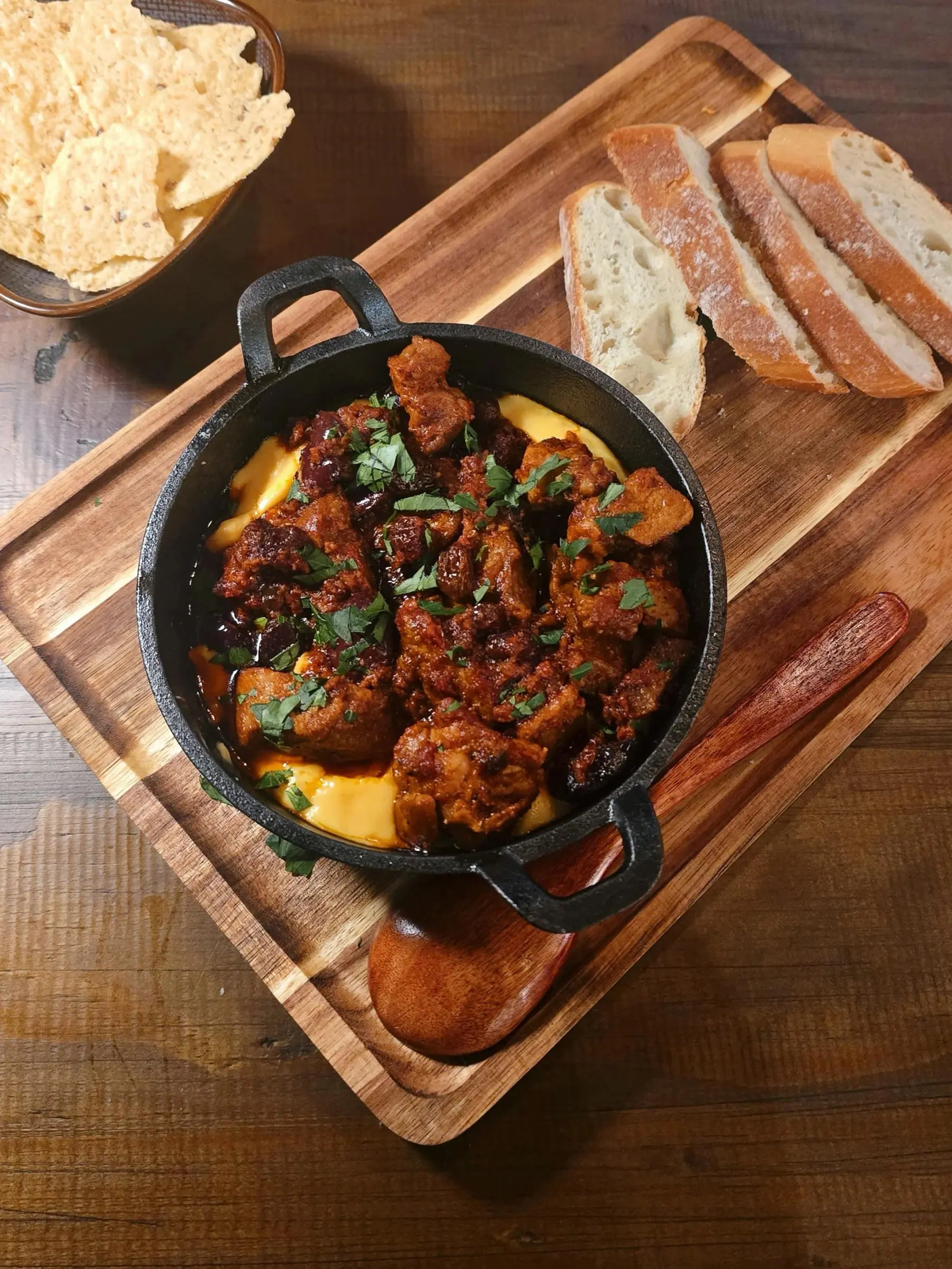 A cast iron dish of braised chorizo and beans with herbs, served with sliced baguette and crisps
