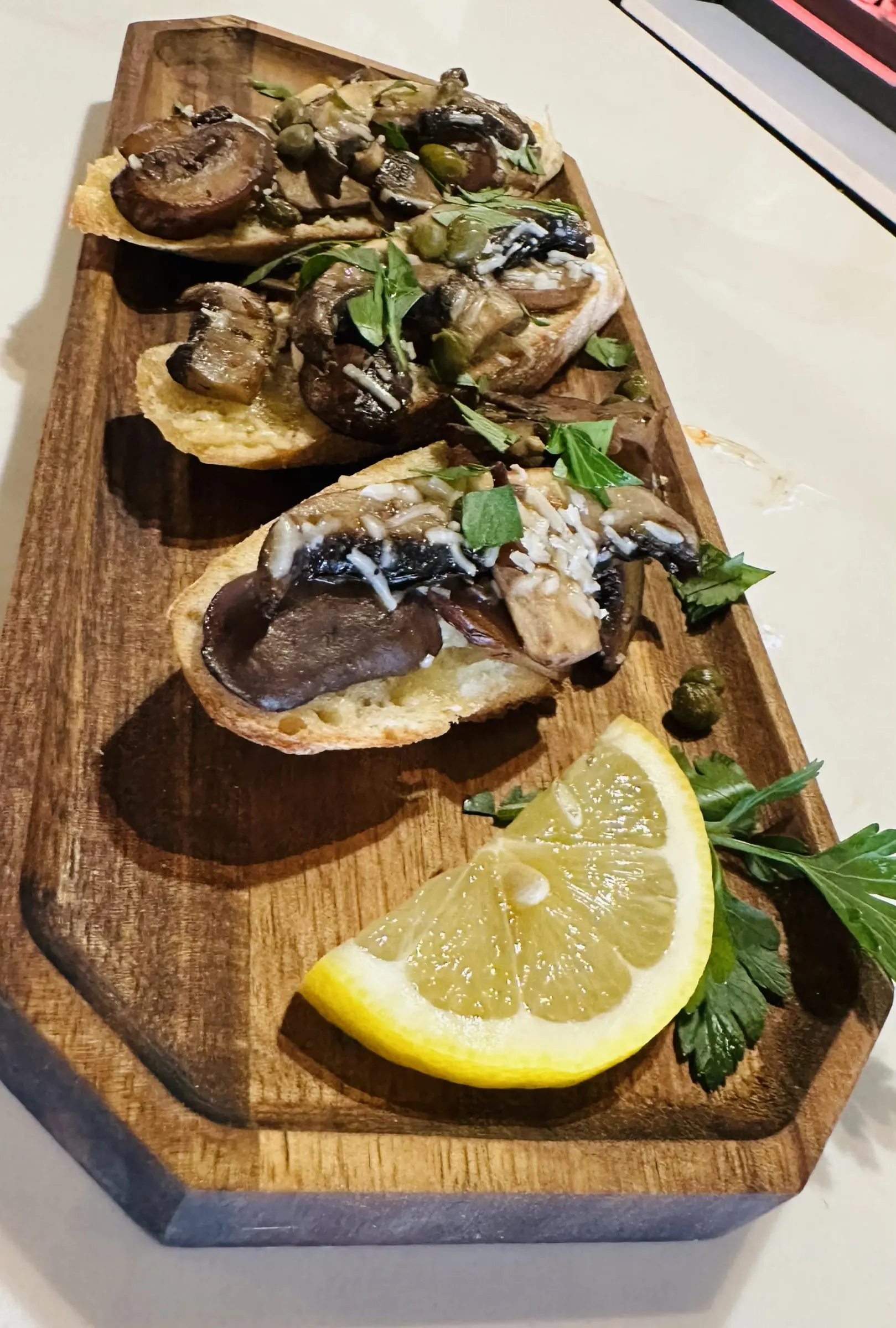 Roasted mushroom and caper crostini arranged on a wooden board with lemon and parsley